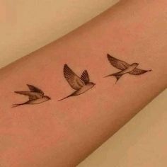 three small birds flying in the air on a woman's right arm, one is black and white