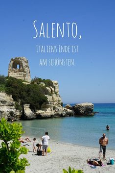 people are on the beach and in the water near an old structure with words written above it