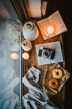 a wooden table topped with doughnuts next to candles and an open book on top of it