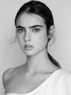 a black and white photo of a young woman with long hair wearing a one shoulder top