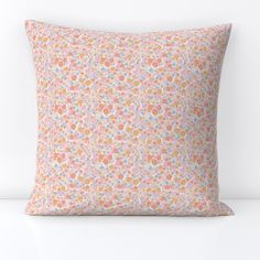 an orange and pink pillow with small flowers on the front, sitting on a white surface