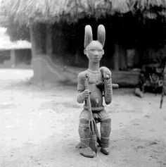 an old black and white photo of a statue in front of a thatched hut