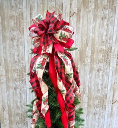 a christmas tree with a red and black bow on it's top, sitting in front of a wooden fence