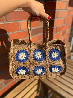 a hand holding a crocheted purse with blue and white flowers on the front