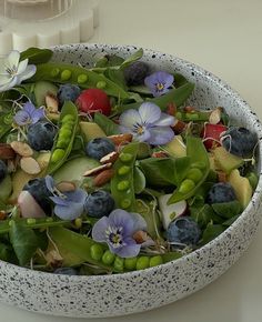 a white bowl filled with lots of different types of vegetables and fruit on top of a table