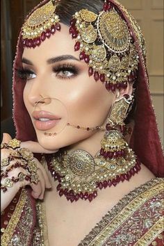 a woman in a red and gold outfit with jewelry on her head, wearing a veil