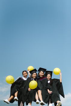 four girls in graduation gowns are holding yellow balloons and jumping up into the air