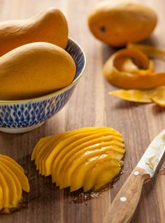 a wooden table topped with sliced mangoes and a bowl filled with orange peels