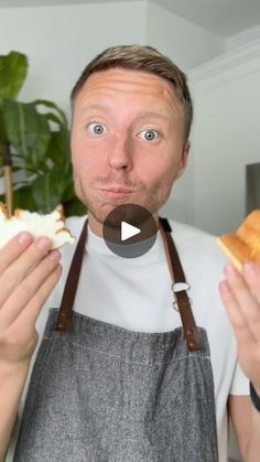 a man in an apron is holding bread and looking at the camera with his mouth wide open