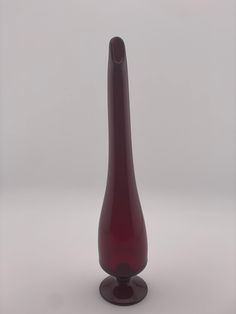 a red glass vase sitting on top of a white table next to a gray wall