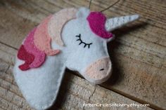 a felt unicorn ornament hanging on a wooden table