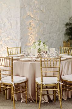 the table is set with gold chairs and white flowers