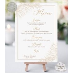 a white and gold wedding menu card on top of a wooden easel with flowers in the background