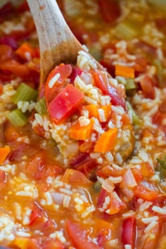 a spoon full of rice and vegetables being stirred with a wooden spoon in a pot