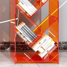 there is a red shelf with books on it in front of a gray wall and marble floor