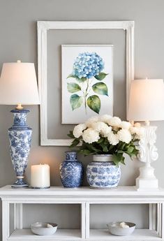 blue and white vases on a table with flowers in front of a framed painting