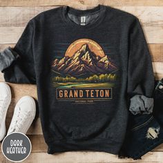 "Show off your love of Wyoming's majestic mountains with our Grand Teton National Park Sweatshirt! This vintage designed crewneck makes a great family vacation trip gift, and is all about embracing the great outdoors! It features a custom sunset design that showcases the unique shape and beauty of the Tetons which the park is known so well for! The Gildan 50/50 blend fabric has that comfy, lived-in feel, that's like a hug every time you put it on! Now you can take a bit of the Tetons with you wherever you go! Grab one now and hit the trail! * Product Highlights * Ideal for any situation, this Gildan 18000 heavy blend crewneck sweatshirt is pure comfort. Made from an extremely soft 50/50 polyester and cotton blend, this combination helps keep you warm and comfortable. The collar features a Winter Crew Neck Tops For Adventure, Graphic Print Crew Neck Tops For Outdoor Activities, Graphic Print Crew Tops, Winter Hiking Crew Neck Top, Outdoor Graphic Print Crew Neck Sweatshirt, Graphic Print Crew Neck Sweatshirt For Outdoor, Relaxed Fit Crew Neck Sweatshirt For Hiking, Outdoor Pre-shrunk Crew Neck Sweatshirt, Relaxed Fit Crew Neck Tops For Hiking