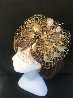 Delicate gold fascinator with scatter of blue crystals, This design can also be made without the blue crystals and be replaced with clear ab crystals ( please note this on your order notes) This design is a beautiful selection of glass effect leaves and wire crystal stems clustered together amongst a fine layer of veiling and set onto a fine comfort base tiara band. As with all our designs, this piece can be made exact to the image or in any colour combination to match in with your outfit. If a Gold Crown Costume Headpiece For Weddings, Gold Crown Headpiece For Evening, Gold Wedding Hat Headband, Gold Headband Hat For Wedding, Gold Costume Hats With Structured Crown For Evening, Elegant Gold Mini Hats For Gifts, Elegant Gold Mini Hats For Gift, Gold Evening Fascinator With Pinched Crown, Gold Pinched Crown Fascinator For Wedding