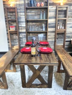 a wooden table with red plates and wine glasses on it in front of some shelves