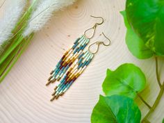 a pair of beaded earrings sitting on top of a table next to a plant