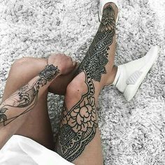 a person with tattoos on their legs sitting on the floor next to a white shoe