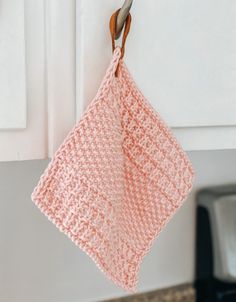 a pink crocheted dish cloth hanging from a hook on a kitchen cabinet door