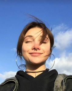 a young woman with her eyes closed and nose piercings up to the camera, smiling