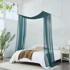 a bed with a blue canopy hanging from it's side in a white room