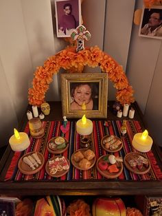 a table topped with candles and pictures next to an orange flower arch filled with food