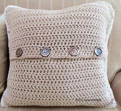 a crocheted pillow with three buttons on the front and back of it, sitting on a couch