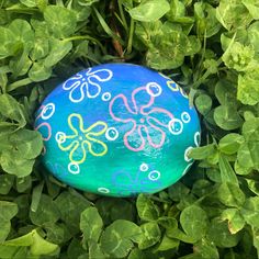 a painted rock in the grass with flowers on it