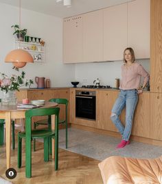 a woman leaning against the wall in a kitchen next to a table with chairs and a couch