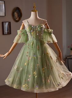 Mellow yet striking, this soft green homecoming dress is a true testament to the art of detailed craftsmanship and design. The gown is adorned with an exquisite array of hand-embroidered flowers, each stitch contributing to a tapestry of floral elegance that seems to whisper tales of springtime serenades. The off-shoulder sleeves crafted from the same sheer material as the overlay add a modern twist to the classic silhouette, providing a flattering look for all who wear it. Beneath the floral embroidery, the dress extends into a full, flowing skirt that promises to sway elegantly at every turn. Perfect for those who appreciate a blend of contemporary fashion and timeless details, this dress ensures you'll look and feel spectacular at your next formal gathering. Enchanted Forest Dress Short, Green Short Prom Dress, Grey Prom Dress Long, Green Silhouette, Floral Homecoming Dresses, Grey Prom Dress, Prom Season, Green Homecoming Dresses, Prom Dresses Yellow