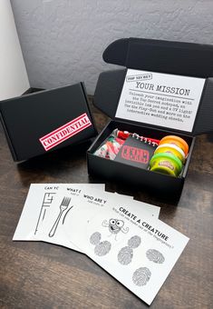 an open box with some items in it on a wooden table next to papers and scissors