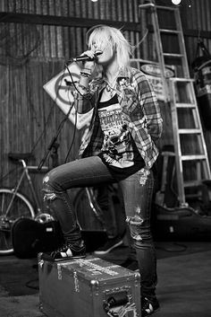 a woman sitting on top of a piece of luggage while holding a microphone to her mouth