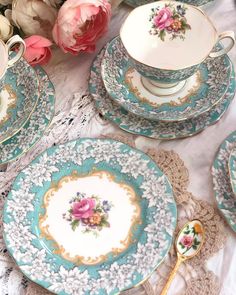 a table topped with blue and white plates covered in flowers next to a vase filled with pink roses