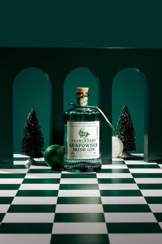 a green bottle sitting on top of a black and white checkered floor next to trees