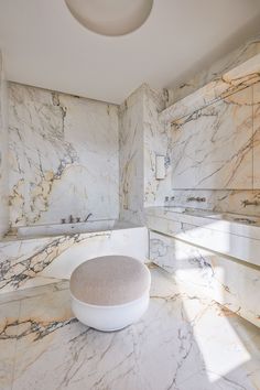 a bathroom with marble walls and flooring, including a round foot stool in the middle