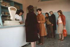 a group of people standing around a counter in a room with blue walls and shelves