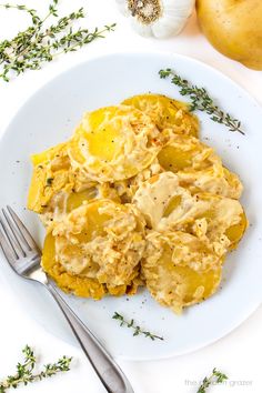 a white plate topped with potatoes covered in gravy next to garlic and onions