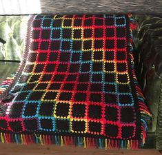 a crocheted blanket sitting on top of a wooden bench next to a window