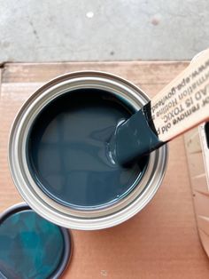 a can of blue paint with a brush in it next to a box of other paints