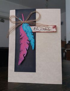 a handmade card with a pink and blue feather hanging from it's side