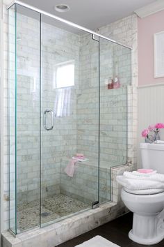 a white toilet sitting next to a walk in shower under a bathroom window with pink towels on the floor