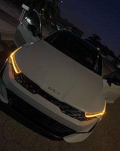 the front end of a white car with its lights on