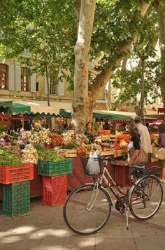 a bicycle parked in front of a fruit and vegetable stand with people shopping at it