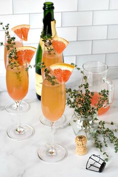 three wine glasses filled with orange slices and garnished with greenery next to two bottles of champagne