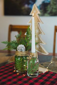 a small christmas tree in a jar next to a candle on a plaid tablecloth