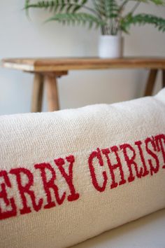 a red merry christmas pillow sitting on top of a white couch next to a potted plant