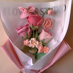 a bouquet of crocheted flowers is wrapped in white paper and tied with pink ribbon